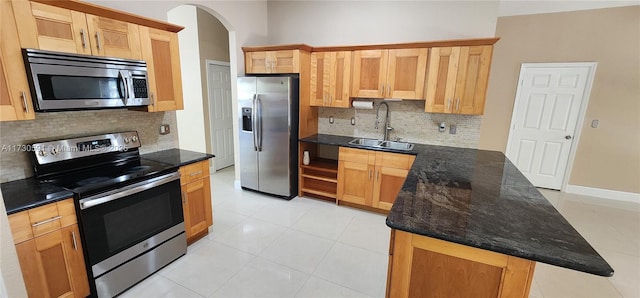 kitchen with sink, light tile patterned floors, appliances with stainless steel finishes, dark stone counters, and decorative backsplash