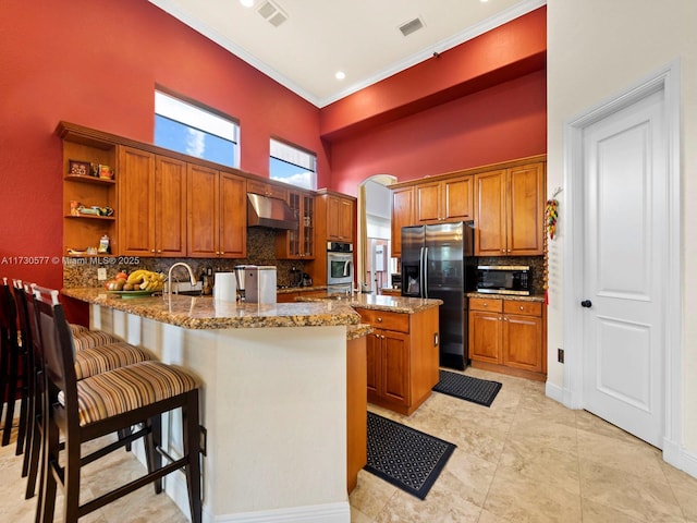 kitchen with appliances with stainless steel finishes, kitchen peninsula, light stone counters, and range hood