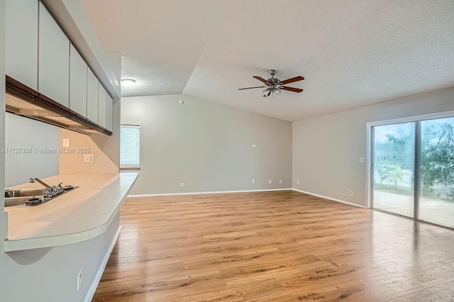 unfurnished living room with a textured ceiling, sink, light hardwood / wood-style flooring, ceiling fan, and lofted ceiling