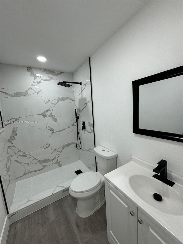 bathroom featuring vanity, hardwood / wood-style flooring, toilet, and tiled shower