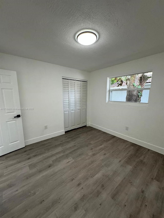 unfurnished bedroom featuring a textured ceiling, dark hardwood / wood-style flooring, and a closet