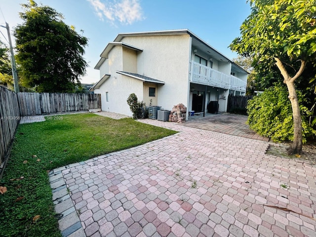 back of house with central air condition unit, a balcony, a yard, and a patio area