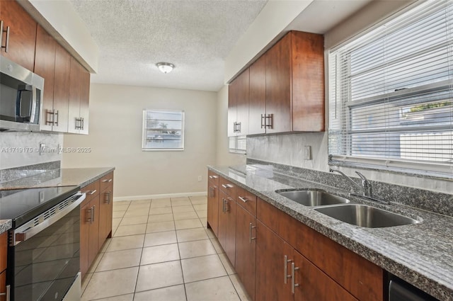 kitchen with a textured ceiling, appliances with stainless steel finishes, dark stone counters, sink, and light tile patterned floors