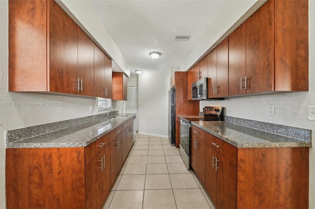 kitchen featuring appliances with stainless steel finishes, sink, dark stone counters, light tile patterned floors, and a textured ceiling