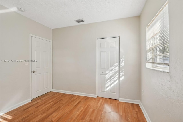 unfurnished room with light hardwood / wood-style flooring and a textured ceiling