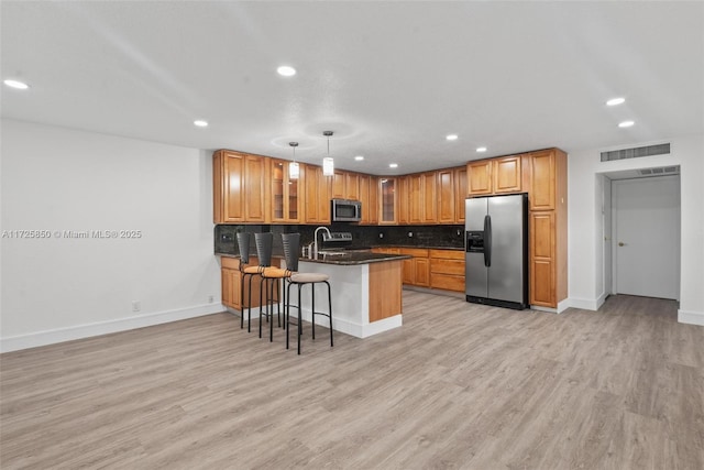 kitchen with a kitchen bar, appliances with stainless steel finishes, light wood-type flooring, kitchen peninsula, and pendant lighting