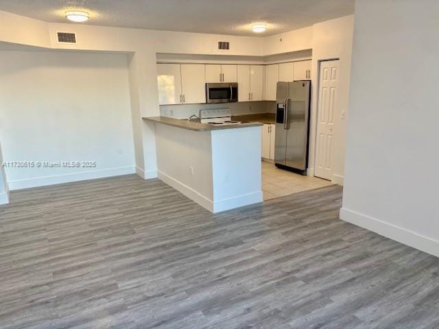 kitchen with white cabinetry, light hardwood / wood-style flooring, kitchen peninsula, and appliances with stainless steel finishes