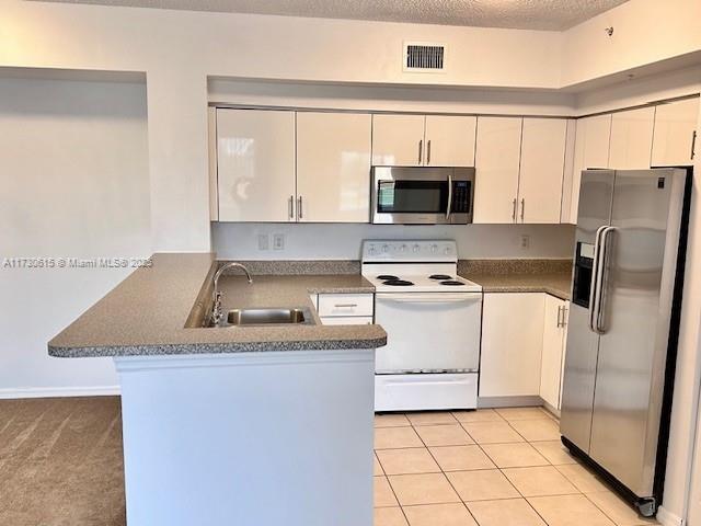 kitchen with sink, appliances with stainless steel finishes, a textured ceiling, white cabinets, and kitchen peninsula