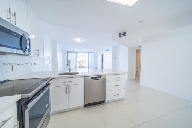 kitchen with appliances with stainless steel finishes, light tile patterned floors, white cabinets, sink, and kitchen peninsula