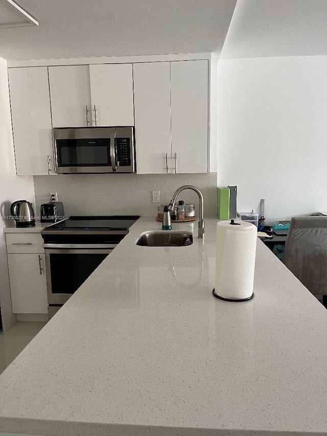 kitchen featuring white cabinets, stainless steel appliances, light stone counters, and sink