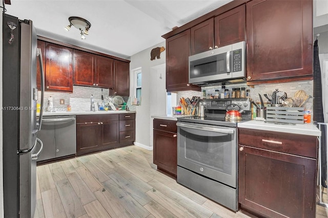 kitchen with appliances with stainless steel finishes, decorative backsplash, light wood-type flooring, and sink