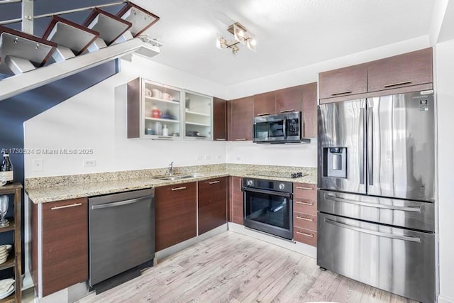 kitchen with light wood finished floors, stainless steel appliances, glass insert cabinets, a sink, and light stone countertops