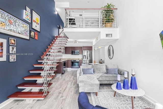 living room featuring visible vents, baseboards, a towering ceiling, light wood-style flooring, and stairway