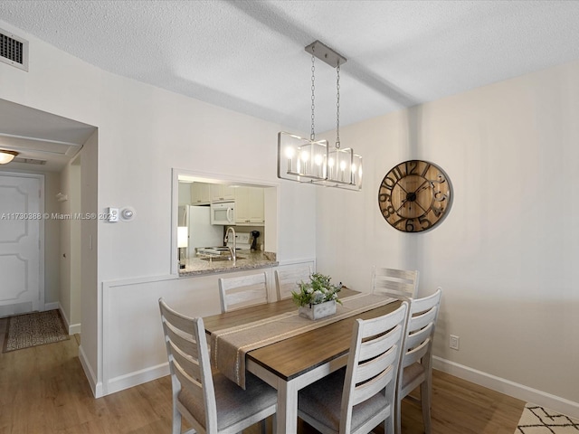 dining area featuring sink, light hardwood / wood-style flooring, and a textured ceiling