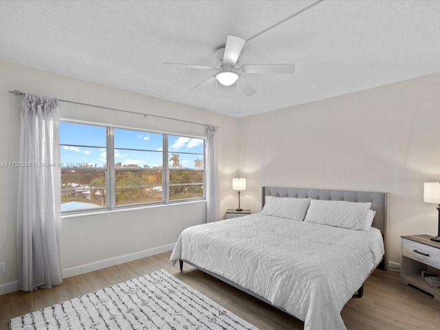 bedroom with ceiling fan, light hardwood / wood-style flooring, a textured ceiling, and multiple windows