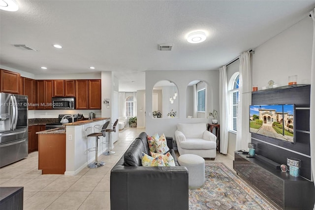 kitchen with a textured ceiling, a kitchen bar, light tile patterned floors, and stainless steel appliances