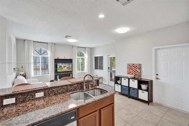 kitchen with stainless steel dishwasher, sink, light tile patterned flooring, a textured ceiling, and dark stone countertops