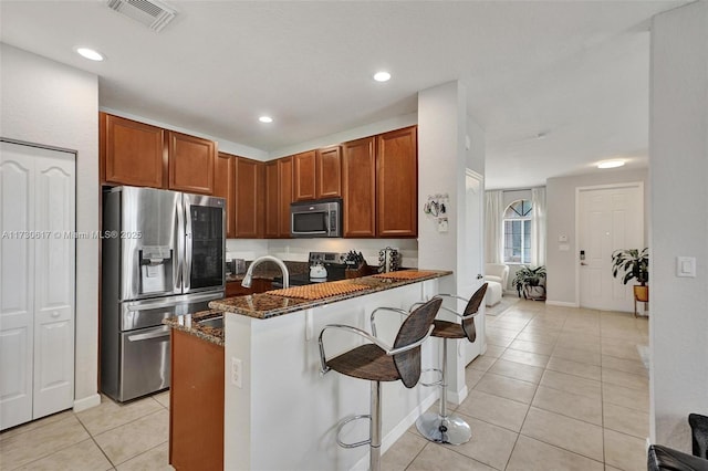 kitchen featuring appliances with stainless steel finishes, a kitchen breakfast bar, kitchen peninsula, dark stone counters, and light tile patterned flooring