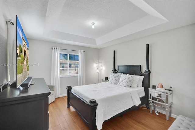 bedroom with light hardwood / wood-style floors, a textured ceiling, and a raised ceiling