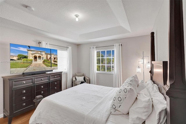 bedroom with a textured ceiling, light hardwood / wood-style flooring, and a raised ceiling