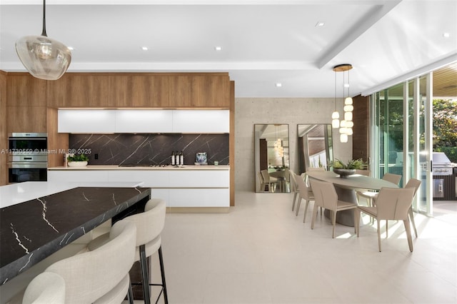 kitchen featuring decorative light fixtures, white cabinetry, double oven, and tasteful backsplash