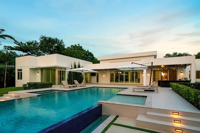 pool at dusk featuring an in ground hot tub and a patio