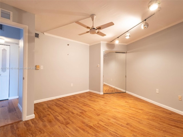 empty room featuring rail lighting, light hardwood / wood-style floors, ceiling fan, and crown molding