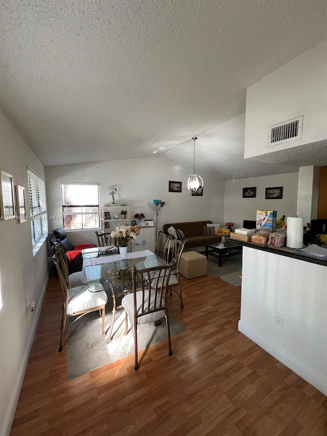 dining room with hardwood / wood-style flooring, lofted ceiling, an inviting chandelier, and a textured ceiling