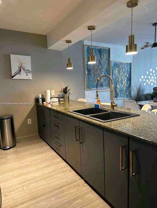 kitchen featuring light wood-style flooring, a sink, baseboards, dark stone counters, and pendant lighting