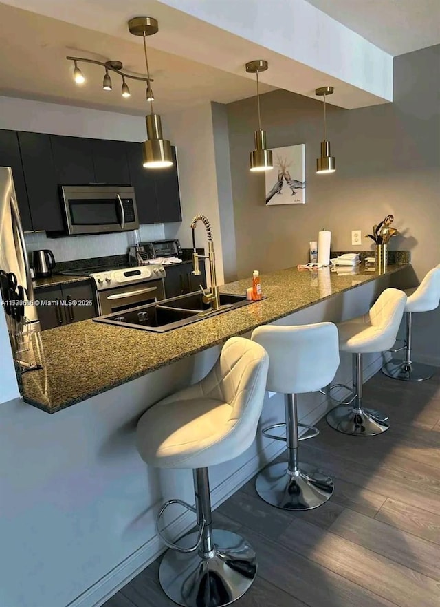 kitchen with a peninsula, dark cabinetry, stainless steel microwave, a kitchen bar, and decorative light fixtures