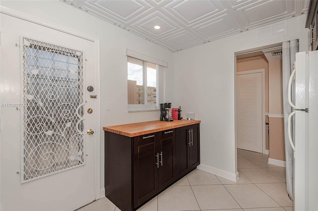 interior space with light tile patterned flooring, dark brown cabinetry, butcher block countertops, and white fridge