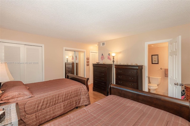 bedroom with light hardwood / wood-style floors, a textured ceiling, connected bathroom, and two closets