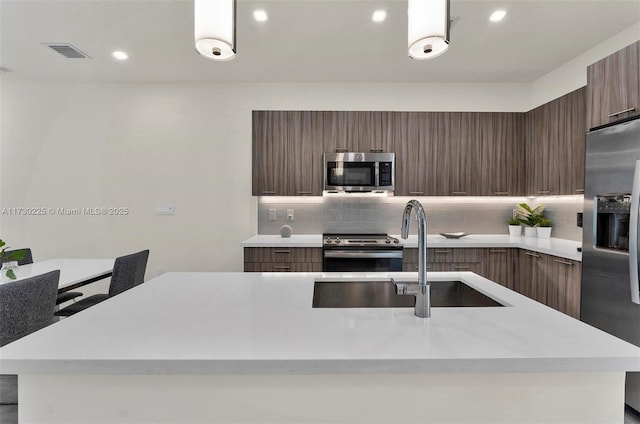 kitchen with sink, an island with sink, appliances with stainless steel finishes, and backsplash