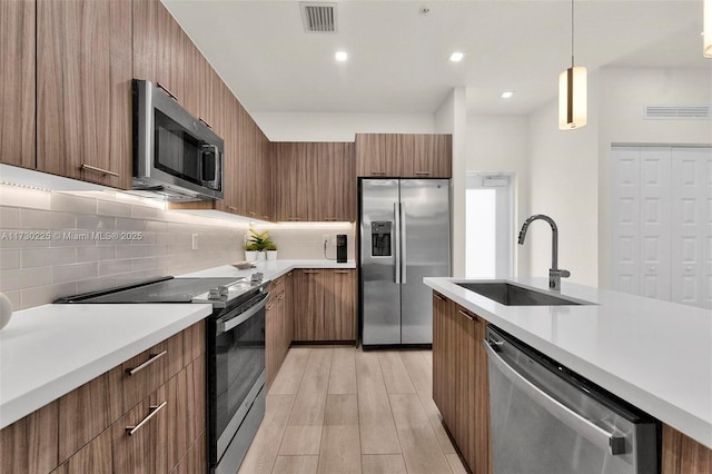 kitchen featuring pendant lighting, appliances with stainless steel finishes, light hardwood / wood-style floors, sink, and backsplash