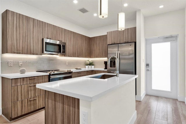 kitchen with sink, stainless steel appliances, pendant lighting, and an island with sink