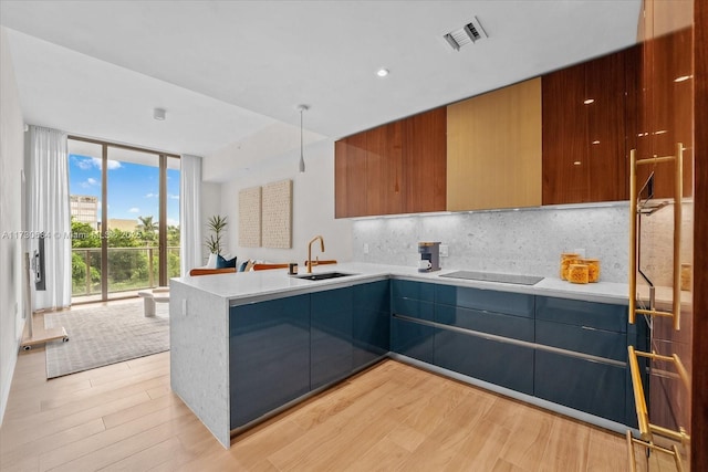 kitchen featuring sink, backsplash, light wood-type flooring, a wall of windows, and black electric cooktop