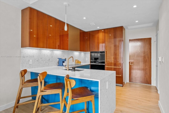 kitchen featuring tasteful backsplash, a kitchen breakfast bar, sink, light hardwood / wood-style flooring, and kitchen peninsula