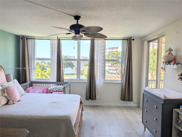 bedroom featuring multiple windows, a textured ceiling, ceiling fan, and light wood-type flooring