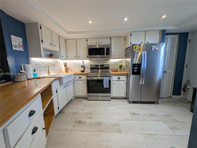 kitchen with white cabinetry, stainless steel appliances, sink, and wooden counters