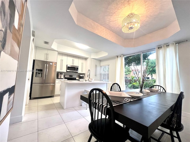 tiled dining area with sink and a tray ceiling