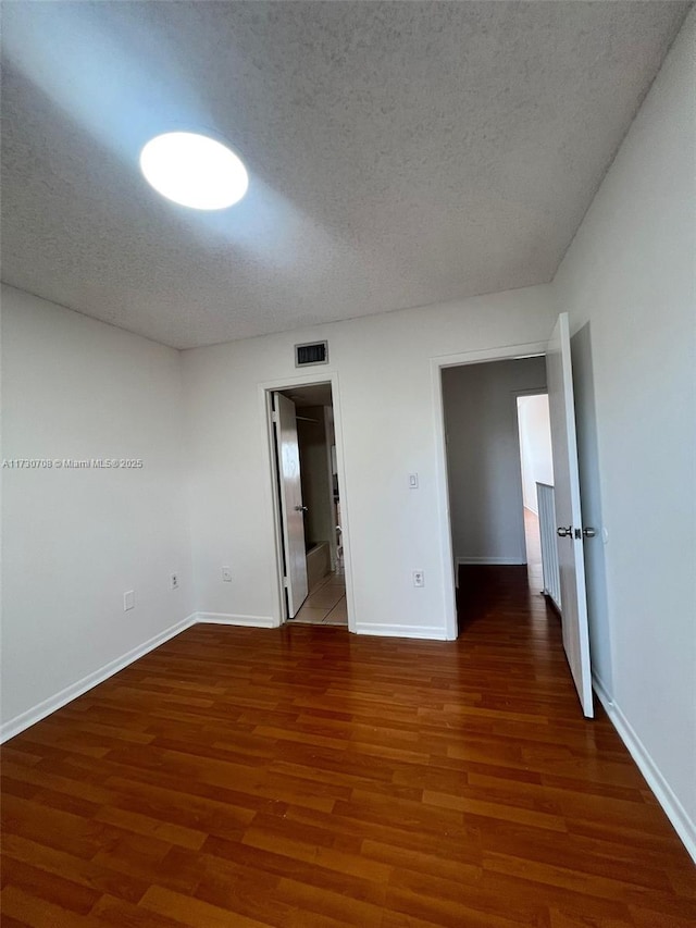 unfurnished bedroom with ensuite bathroom, dark wood-type flooring, and a textured ceiling