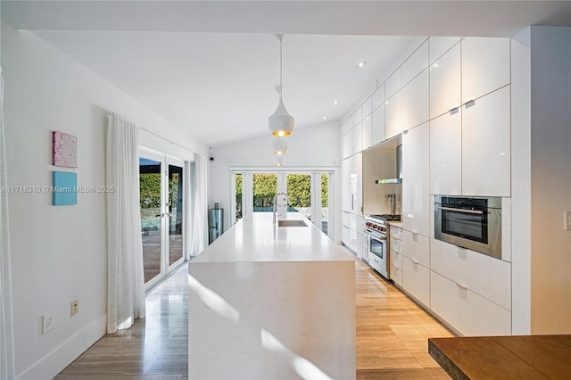 kitchen with pendant lighting, white cabinets, stainless steel appliances, french doors, and an island with sink