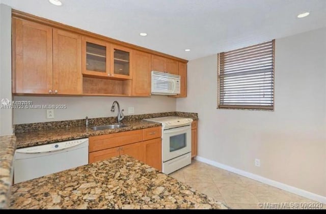 kitchen featuring sink, white appliances, light tile patterned floors, and dark stone countertops