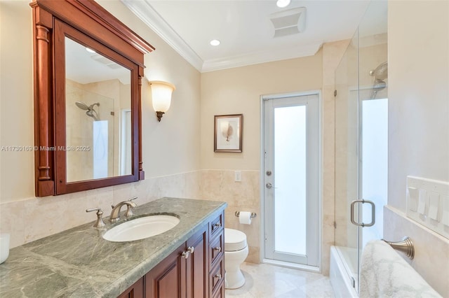 full bathroom featuring tile walls, shower / bath combination with glass door, vanity, toilet, and crown molding