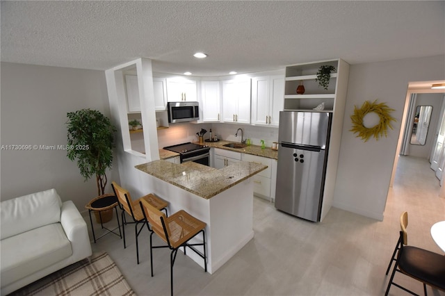 kitchen featuring white cabinetry, appliances with stainless steel finishes, a kitchen bar, and kitchen peninsula