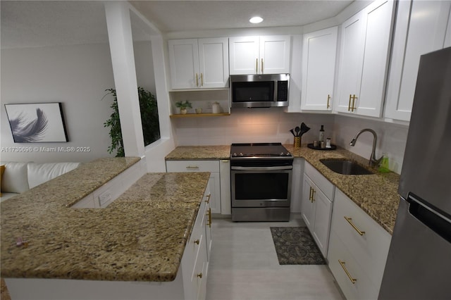 kitchen with sink, white cabinets, light stone counters, kitchen peninsula, and stainless steel appliances