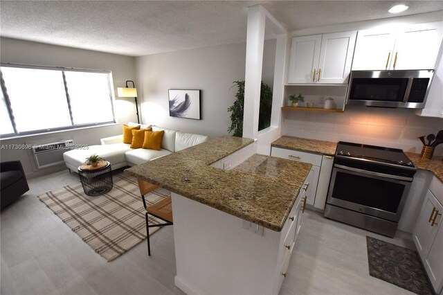 kitchen with a wall mounted air conditioner, tasteful backsplash, white cabinets, stainless steel appliances, and light stone countertops