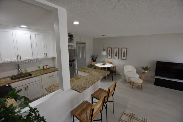 kitchen with sink, a kitchen breakfast bar, white cabinets, a textured ceiling, and decorative light fixtures