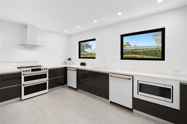 kitchen with white appliances, wall chimney range hood, tasteful backsplash, sink, and light tile patterned floors