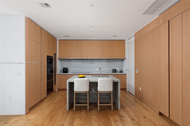 kitchen featuring a kitchen bar, an island with sink, light hardwood / wood-style flooring, and light brown cabinets